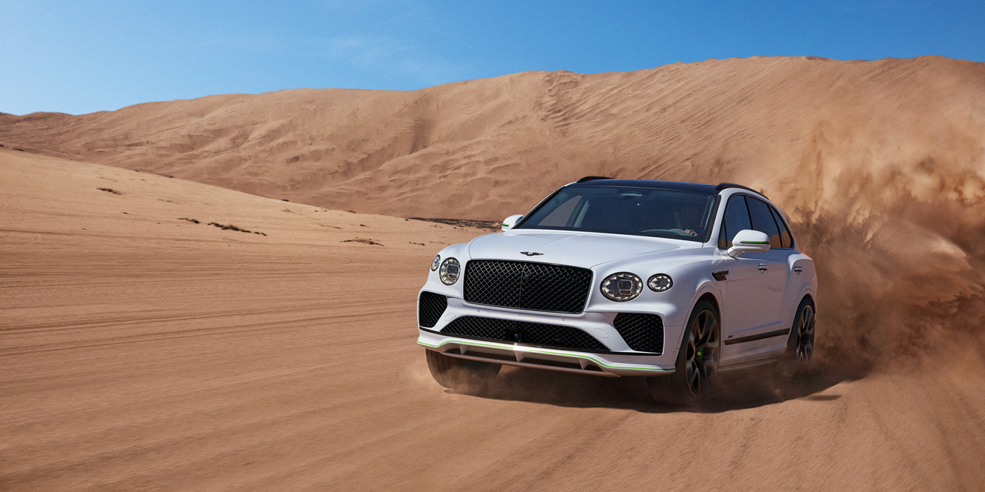 Bentley Düsseldorf Bentley Bentayga Speed SUV front three quarter in Snow Quarts Pearlescent by Mulliner white paint driving dynamically through the desert