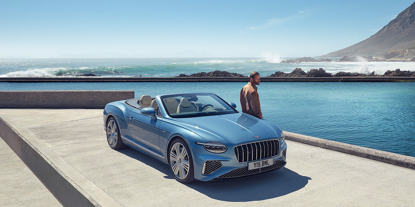 Bentley Düsseldorf New Bentley Continental GTC Azure convertible front view in Light Windsor blue paint with 22 inch ten spoke wheels parked by the sea in the sunshine