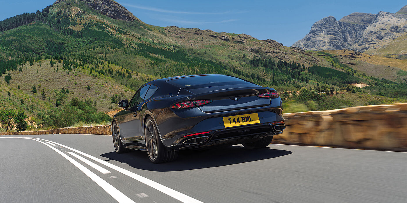 Bentley Düsseldorf Bentley Continental GT Coupé in Thunder Lackierung, Heckansicht bei der Fahrt durch die Berge im Sonnenschein