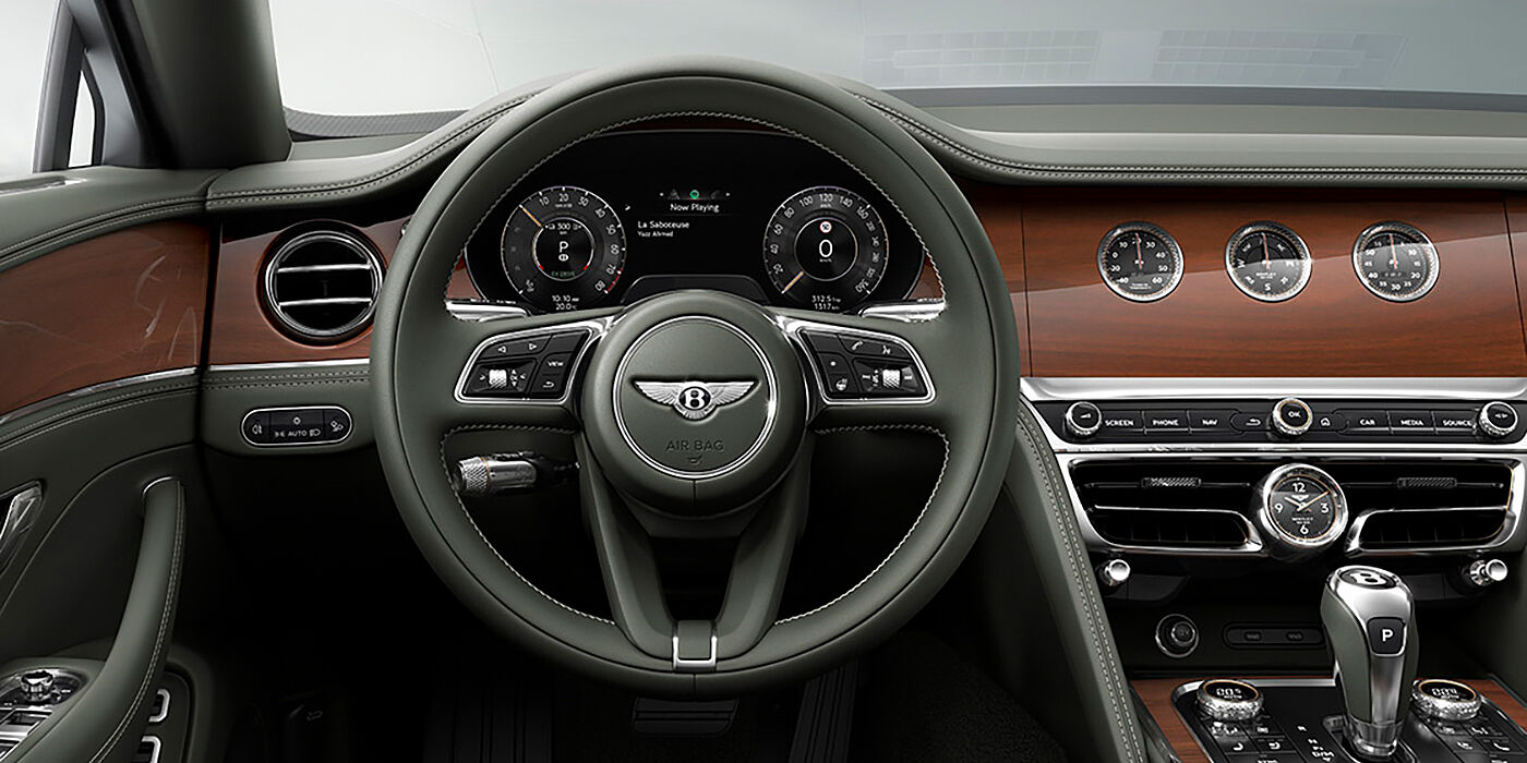 Bentley Düsseldorf New Bentley Flying Spur sedan front cabin in Cumbrian Green hide and Crown Cut walnut veneer showing steering wheel and Rotating Display with three clocks on face