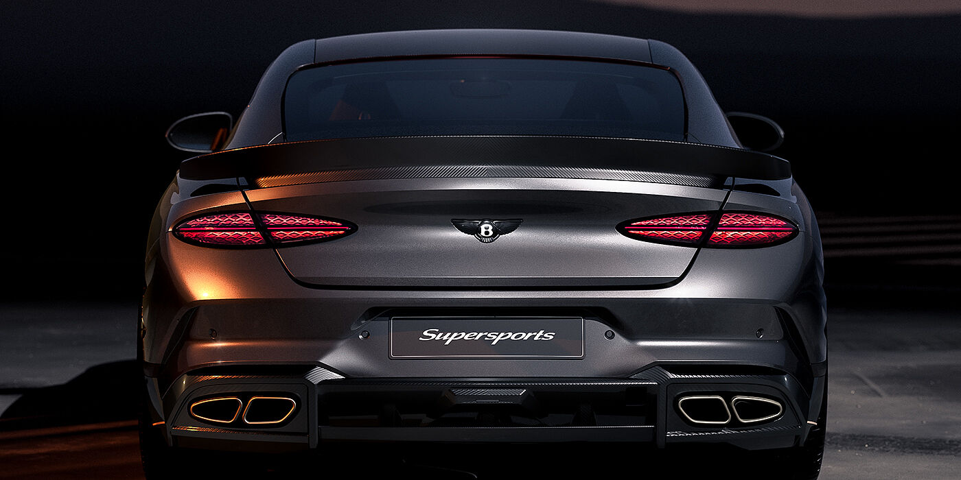 Bentley Düsseldorf Bentley Supersports rear view with illuminated rear lamps, spoiler and black Bentley badge in Anthracite paint against a dark grey and red background