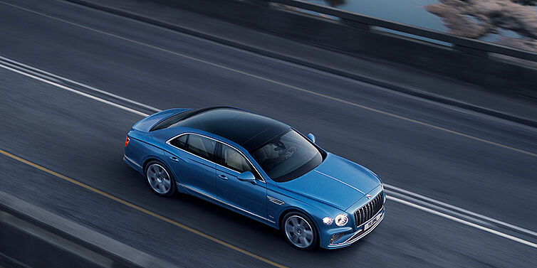 Bentley Düsseldorf New Bentley Flying Spur Azure sedan in Light windsor blue paint by Mulliner, with 22 inch Azure wheels seen from overhead driving dynamically on a country road