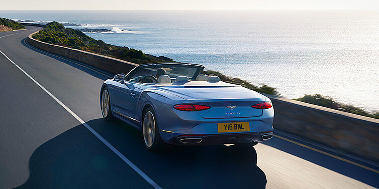 Bentley Düsseldorf New Bentley Continental GTC Azure convertible rear view in Light Windsor blue paint with 22 inch ten spoke wheels driving dynamically on an ocean road in the sunshine