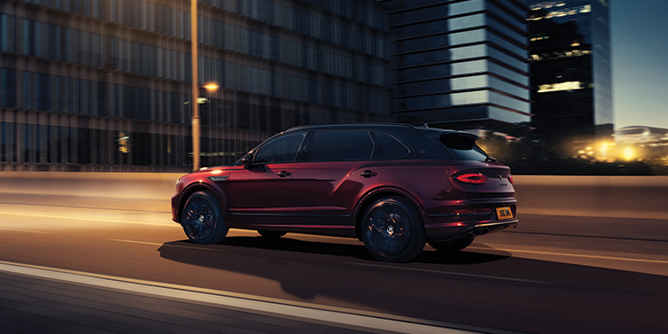 Bentley Düsseldorf Bentley Bentayga Extended Wheelbase Mulliner SUV in Cricket Ball red paint driving dynamically in city at night